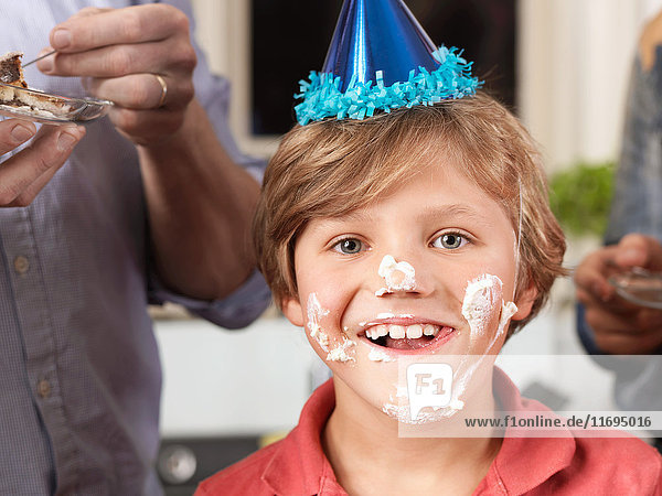 Porträt eines Jungen mit Partyhut und Kuchen im Gesicht