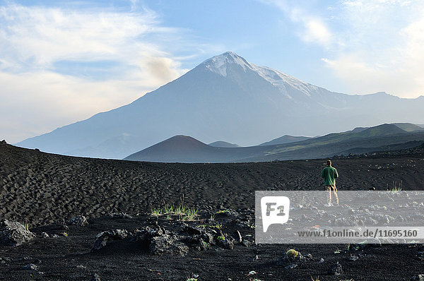 Im Lavafeld stehender Mann mit dem Vulkan Tolbachik im Hintergrund  Halbinsel Kamtschatka  Russland
