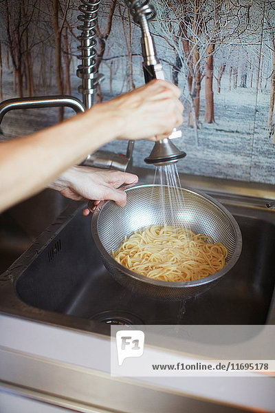 Hands rinsing pasta in sink