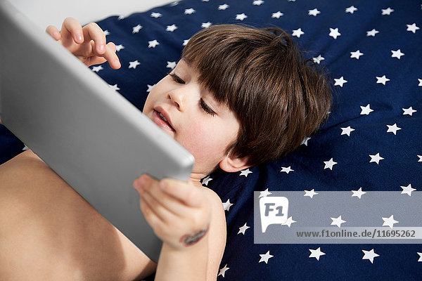 Junge auf dem Bett liegend und mit digitalem Tablett