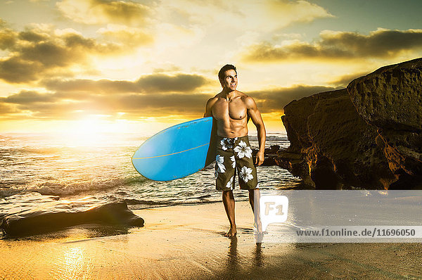 Mann trägt Surfbrett an felsigem Strand