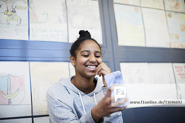 Smiling middle school girl using mobile phone against drawings in corridor