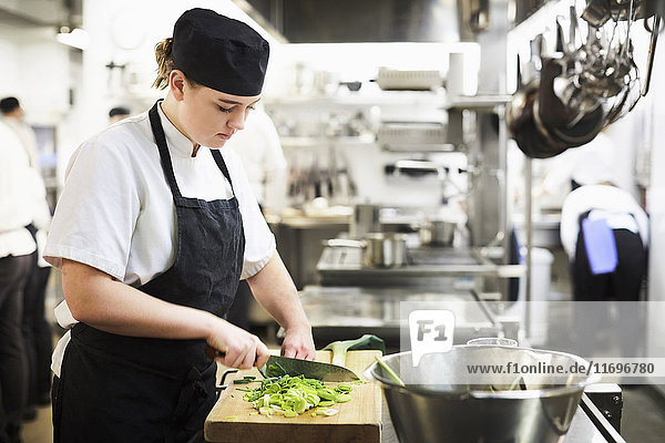 Young female chef chopping vegetables on cutting board in cooking school
