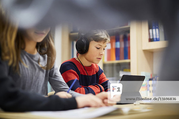 Boy wearing headphones while looking at digital tablet in classroom