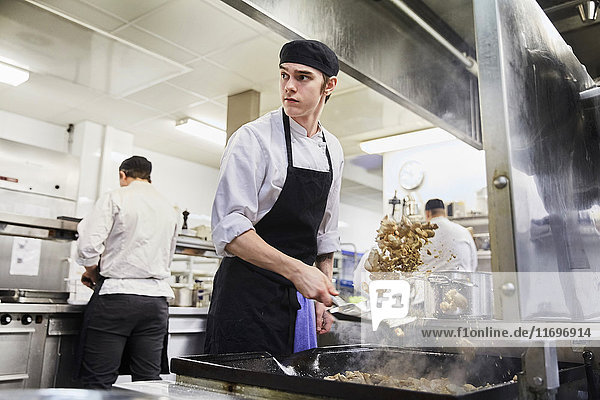 Kochstudent wirft Fleisch mit Kollegen im Hintergrund in der Kochschule