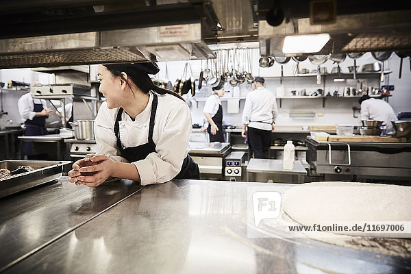 Female chef leaning on counter with colleagues in background at commercial kitchen