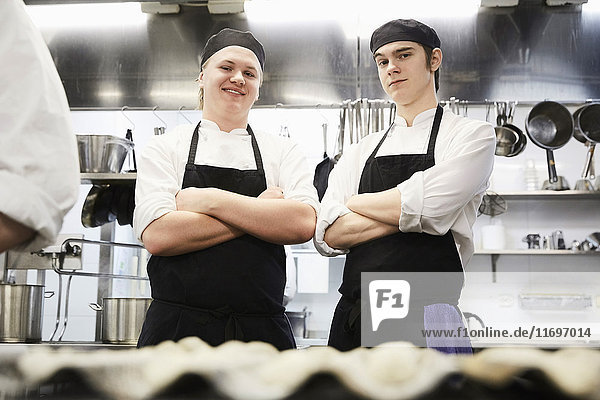 Porträt von lächelnden männlichen Kochstudenten  die in der Großküche gekreuzt stehen.