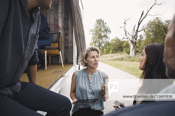 Geschäftsfrau mit digitalem Tablett im Gespräch mit Kollegen per tragbarem Bürowagen