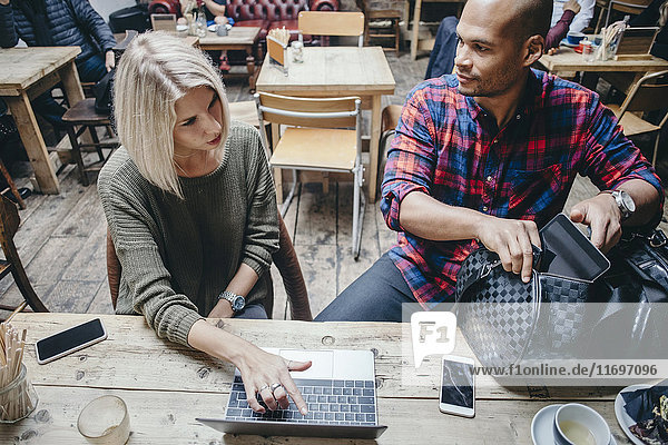 Woman using laptop while discussing with man in coffee shop