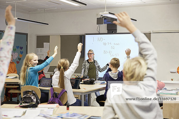 Lehrer betrachtet Schüler mit erhobenen Händen im Klassenzimmer