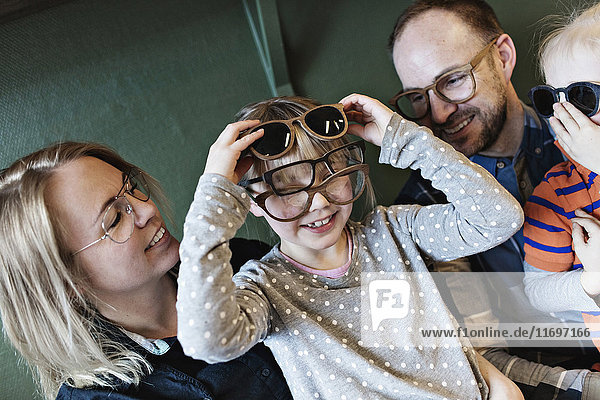 Glückliche Familie beim Anblick des Mädchens mit verschiedenen Brillen im Gesicht in der Werkstatt