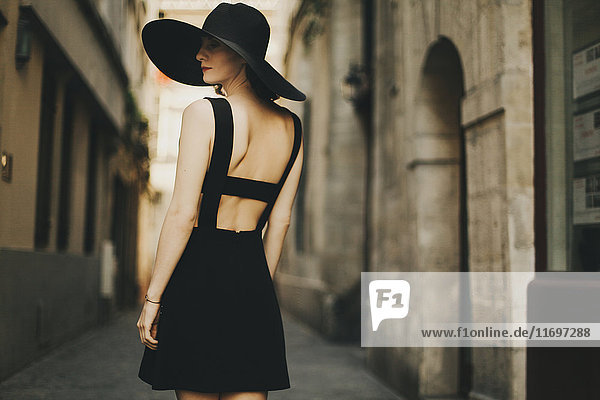 Kaukasische Frau in schwarzem Kleid und Sonnenhut auf der Straße