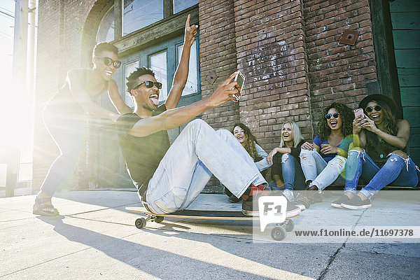 Woman pushing friend sitting on skateboard in city