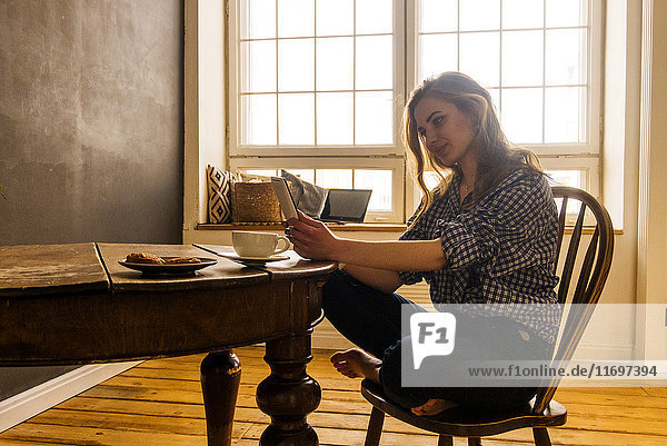 Kaukasische Frau  die am Tisch ein digitales Tablet liest