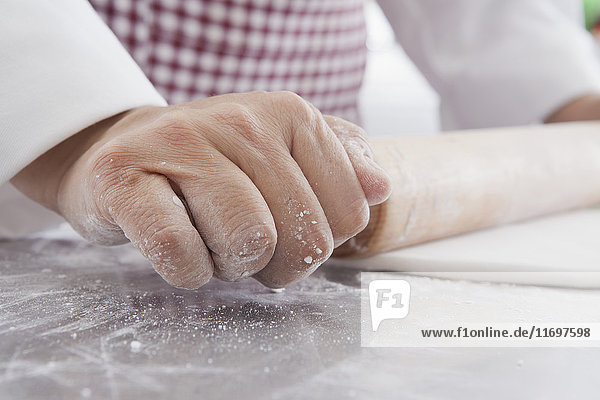 Hands of Hispanic woman using rolling pin on dough
