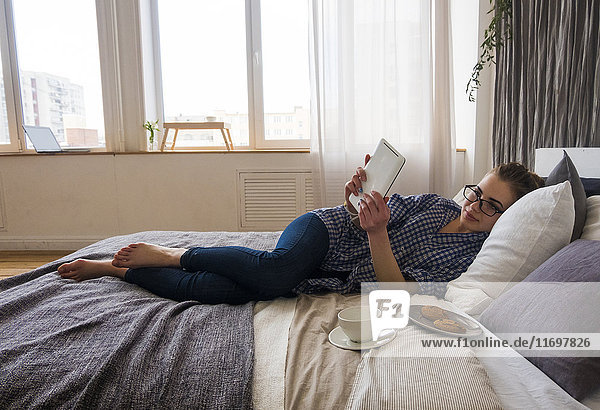 Kaukasische Frau liegt auf dem Bett und liest auf einem digitalen Tablet