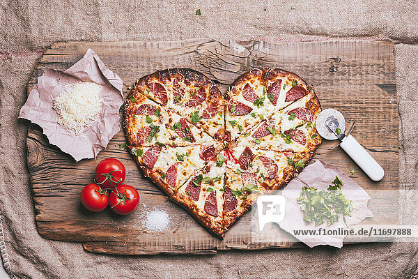 Herzförmige Pizza und Zutaten auf dem Schneidebrett