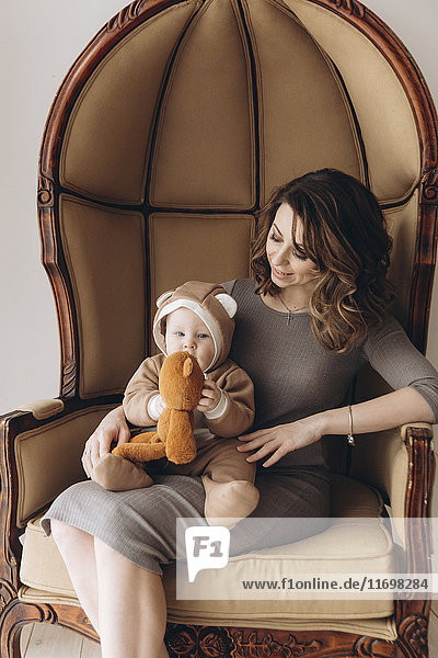 Caucasian mother sitting in armchair with baby son wearing bear costume