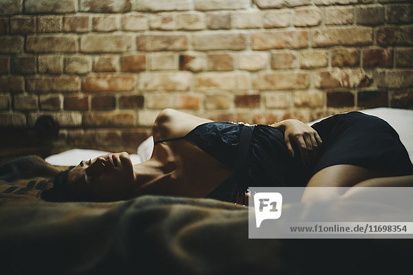 Caucasian woman laying on bed near brick wall