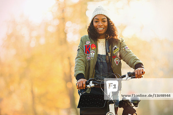 Portrait smiling young woman with bicycle in front of autumn trees