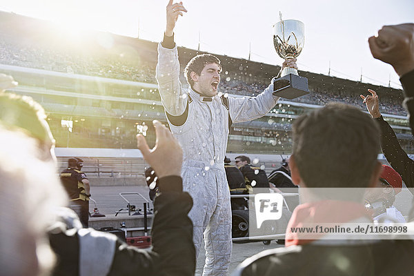 Formula one racing team cheering for driver with trophy  celebrating victory on sports track
