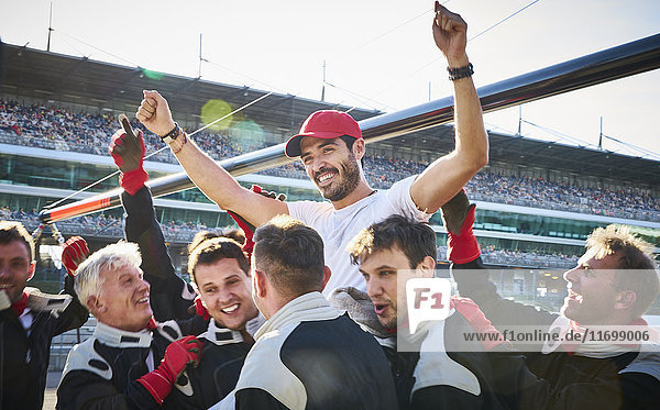 Formula one racing team carrying driver on shoulders  celebrating victory