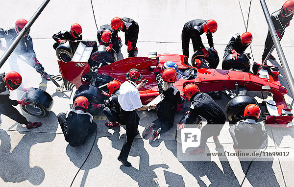 Manager with stopwatch timing pit crew replacing tires on formula one race car in pit lane