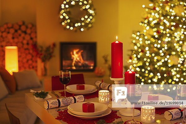 Ambient candles and Christmas crackers on dinner table in living room with fireplace and Christmas tree