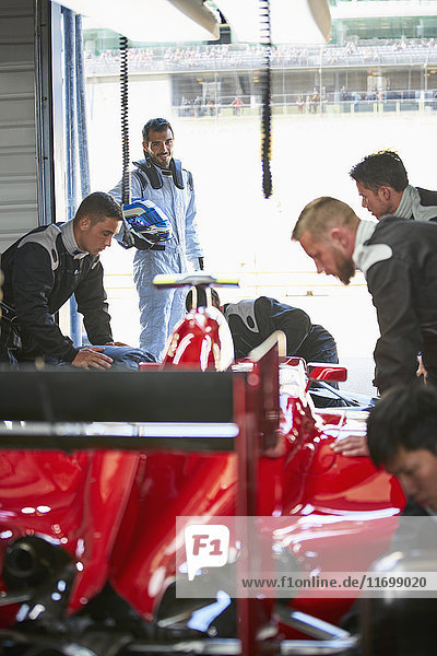 Formula one driver watching pit crew working on race car in repair garage