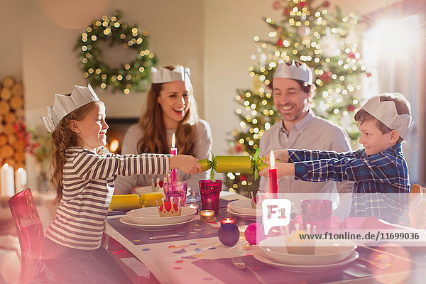 Familie mit Papierkronen  die am Esstisch an Weihnachtsgebäck zieht