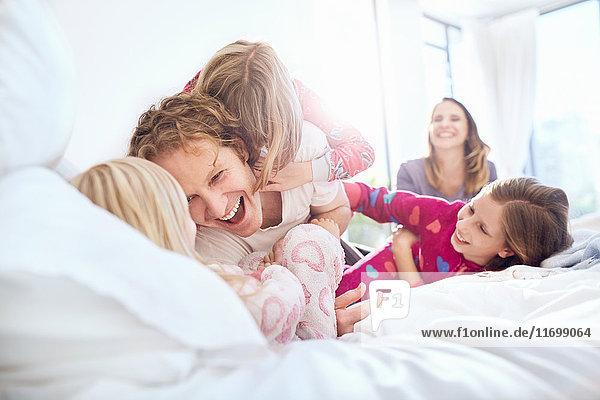 Verspielter Vater und Töchter kitzeln auf dem Bett