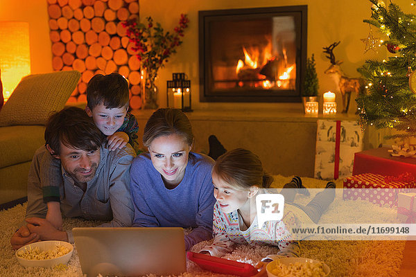Familie isst Popcorn und sieht sich ein Video auf dem Laptop im weihnachtlichen Wohnzimmer mit Kamin an