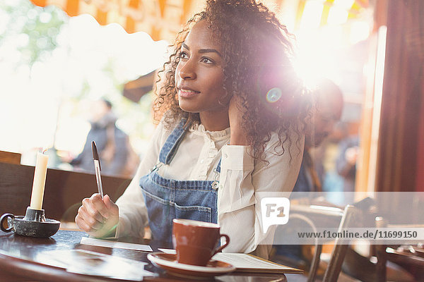 Nachdenkliche junge Frau schreibt Postkarte am Kaffeetisch