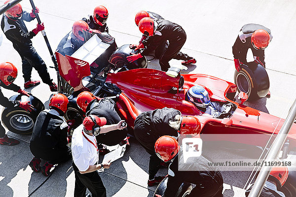 Manager with stopwatch timing pit crew replacing tires in pit lane