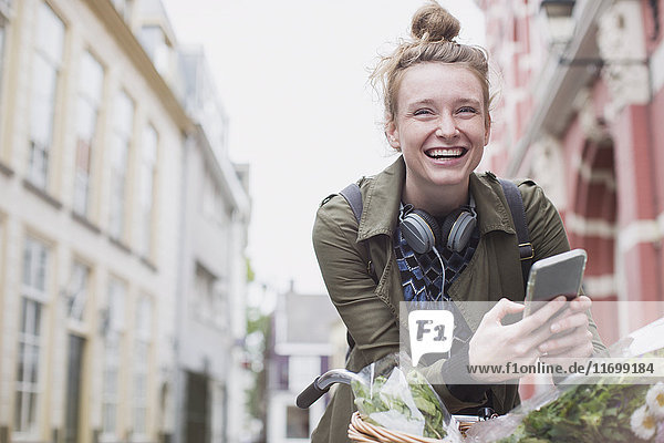 Porträt einer begeisterten jungen Frau auf dem Fahrrad  die auf einer Stadtstraße eine SMS schreibt