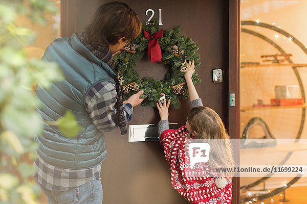 Vater und Tochter hängen Weihnachtskranz an die Haustür
