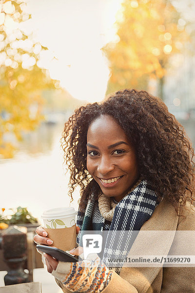 Portrait lächelnde junge Frau trinkt Kaffee und SMS mit Handy im städtischen Straßencafé