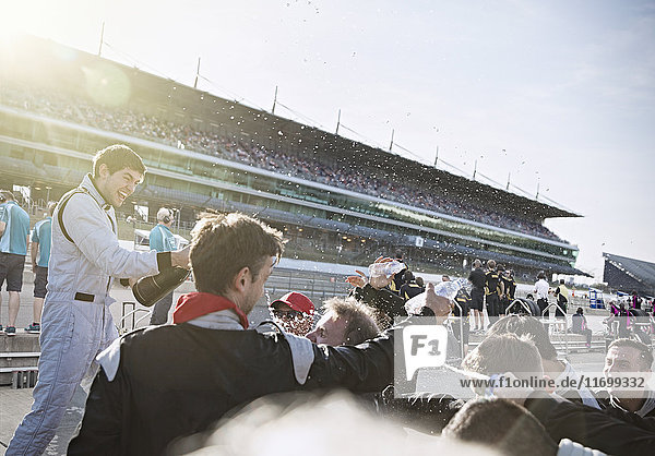 Formula one racing team and driver spraying champagne  celebrating victory on sports track
