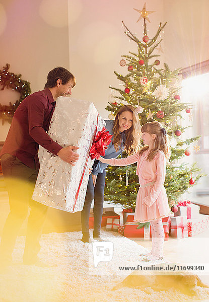 Eltern schenken ihrer Tochter ein großes Weihnachtsgeschenk im Wohnzimmer neben dem Weihnachtsbaum