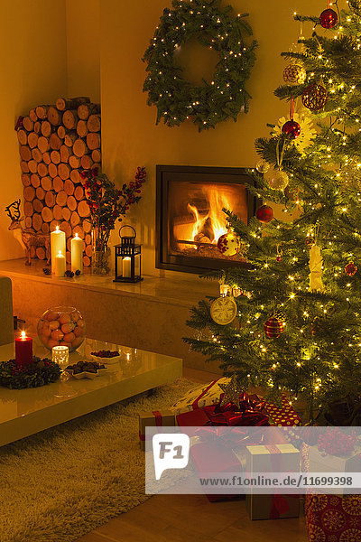 Kaminfeuer und Kerzen beleuchten das Wohnzimmer mit Weihnachtsbaum und -schmuck