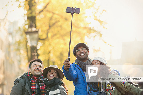 Lächelndes junges Paar Freunde  die Selfie mit Selfie Stick auf der Herbststraße nehmen.