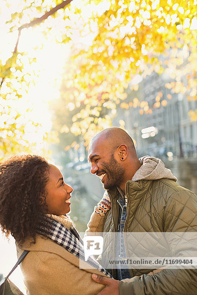 Smiling  affectionate young couple hugging under sunny autumn tree