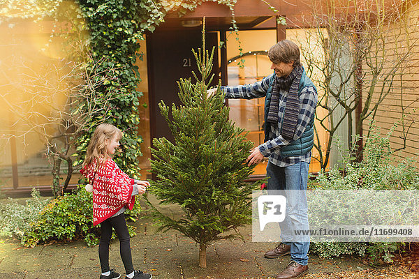 Vater und Tochter mit Weihnachtsbaum vor dem Haus