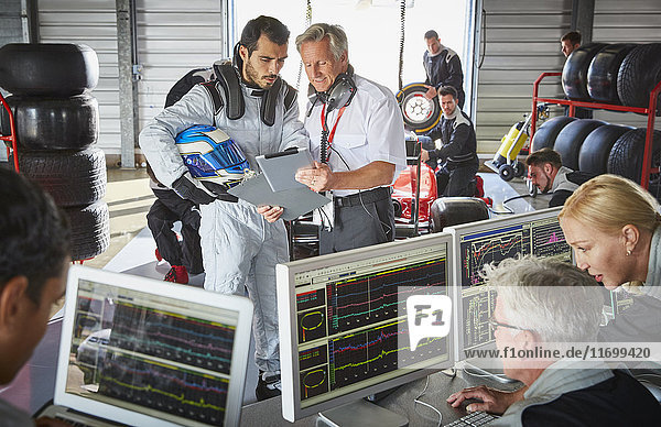 Manager and formula one driver discussing telemetry diagnostics in repair garage