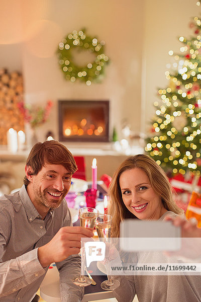 Lächelndes Paar trinkt Champagner und macht ein Selfie am Weihnachtstisch