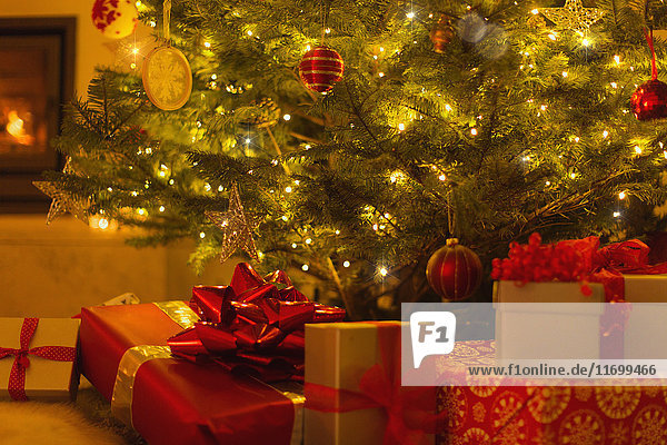 Geschenke mit roten Schleifen unter dem beleuchteten Weihnachtsbaum