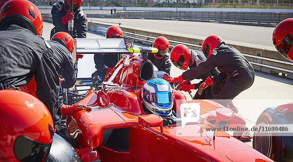 Pit crew replacing tires on formula one race car in pit lane