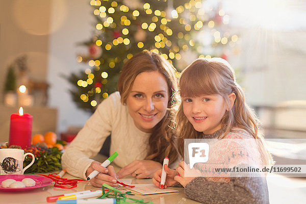 Portrait smiling mother and daughter coloring with markers in Christmas living room