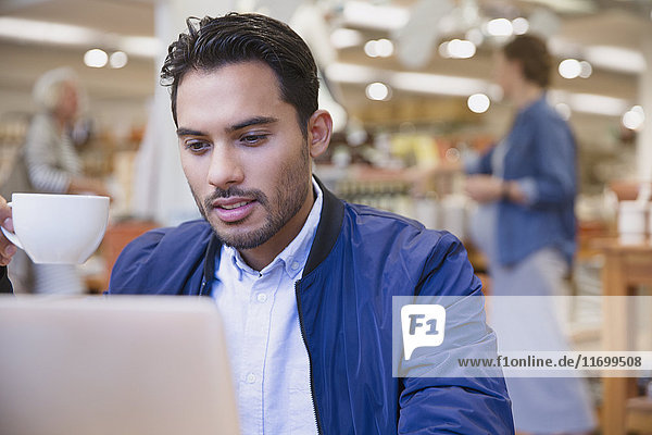 Young man drinking coffee at laptop in cafe