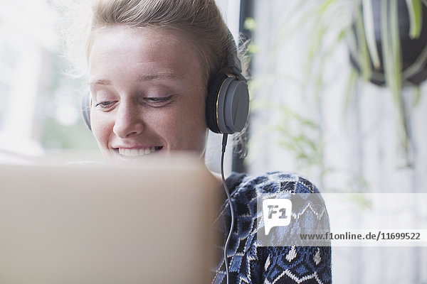 Lächelnde junge Frau mit Kopfhörern und Laptop in einem Café
